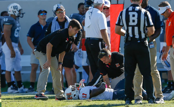 An injured Mercer football player being evaluated on the field by surrounding personnel