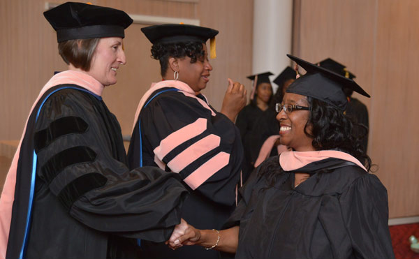 Students in line during commencement with one student shaking hands with a professor