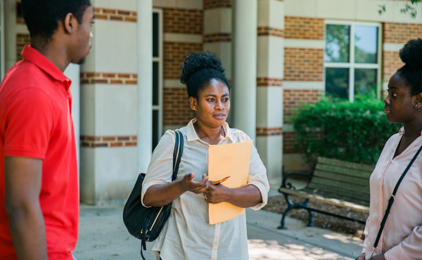 One person holding an envelope and talking to two other people